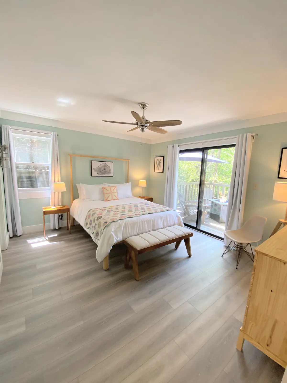A serene bedroom scene with a comfortable bed positioned beside a window, a bench, and soft artwork. The setup is tranquil, with natural light streaming in, suggesting a restful spot to unwind and connect with the natural surroundings.