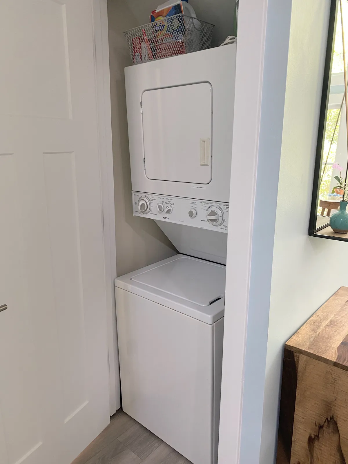 A practical laundry nook with stacked washer and dryer, a basket for laundry supplies, and a clean, organized wooden surface beside the appliances. The setup blends seamlessly into the home, offering everyday convenience.