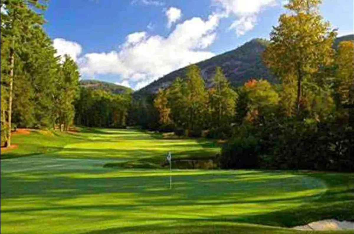 A sprawling green golf course with rolling hills is bordered by trees and set against a picturesque backdrop of distant mountains and drifting clouds. The scene is tranquil, spacious, and welcoming—a wide-open invitation to roam and discover.