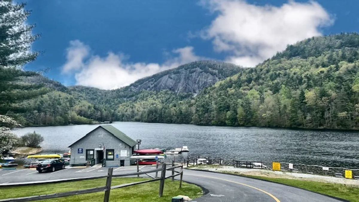 A peaceful lake bordered by a boathouse and mountains, with kayaks ready at the shoreline. The serene water reflects the sky, and the scene hints at a variety of recreational activities available just minutes away.
