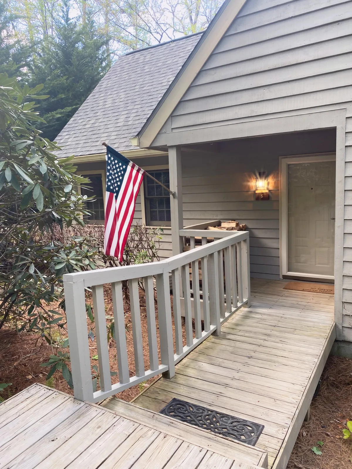An inviting exterior shot of the townhome’s front entrance, complete with a wooden ramp, American flag, outdoor lighting, and lush landscaping. The welcoming porch hints at a warm return after a day of exploration, emphasizing easy access and comfort for all guests.